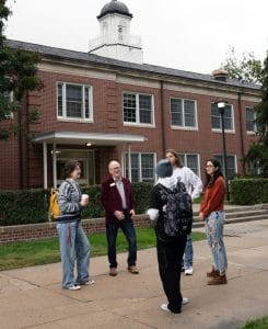 President of college with students in front of a brick building.