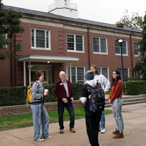 President of college with students in front of a brick building.